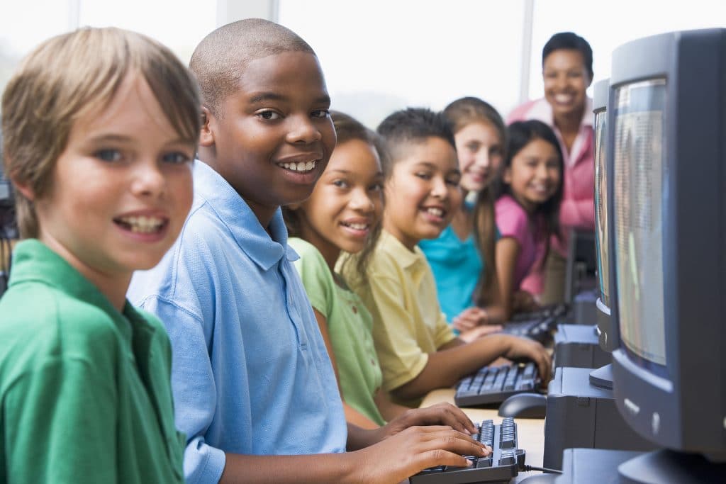 Six children at computer terminals with teacher
